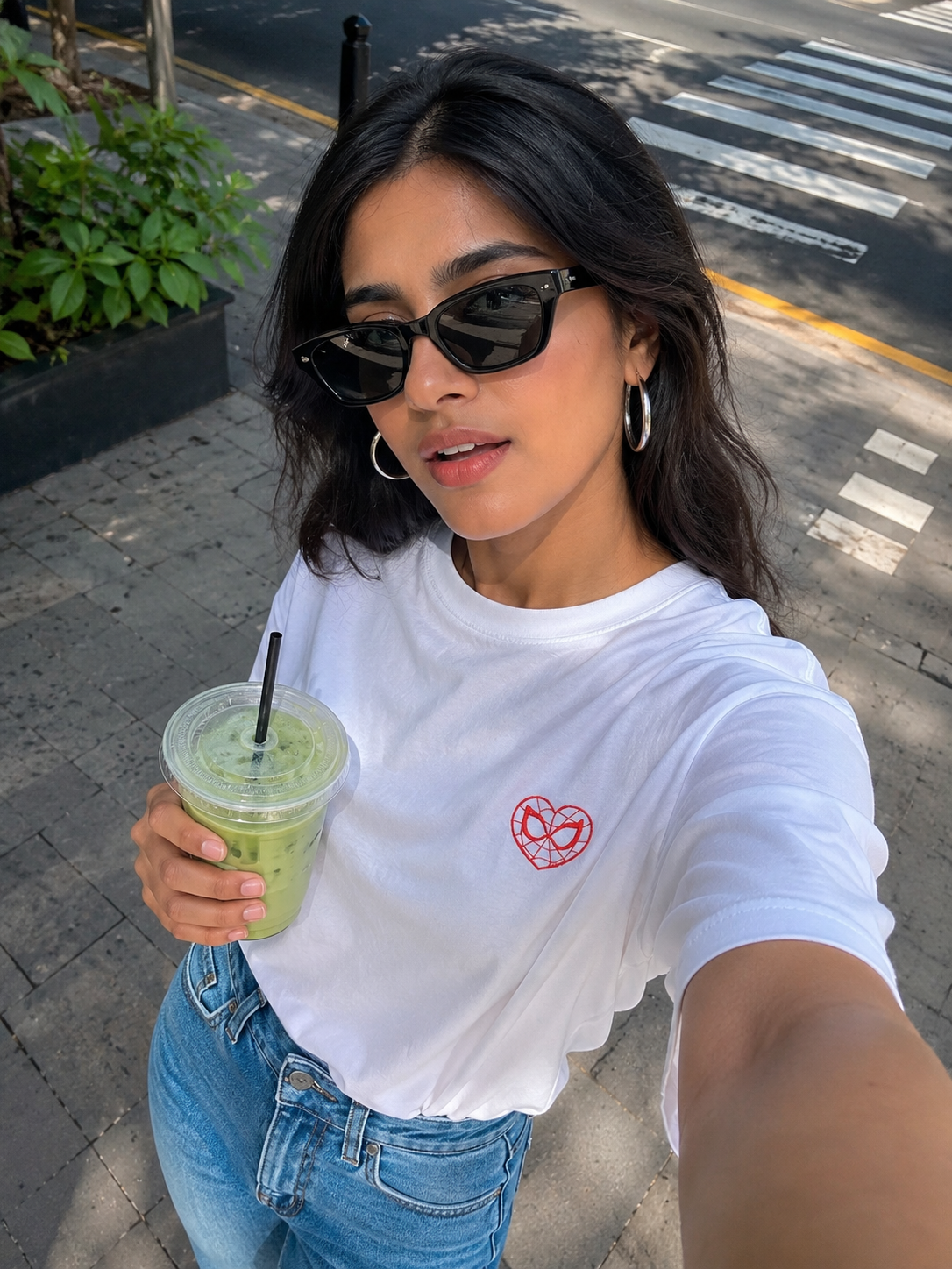 Woman holding a green drink and wearing a white t-shirt with a red logo on a street.